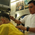 Ángel Orlando Yuca dibuja unos diseños tribales sobre las patillas de Raúl Puchadas en la Peluquería Mi Alborada.