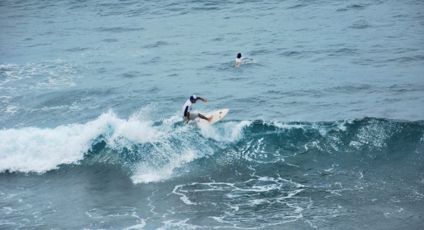 Felipe Rodríguez practica surf en la playa de la FAE en Salinas. Su hijo aparece atrás buscando una ola.